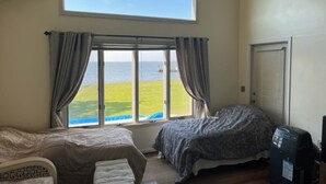A bedroom with a large window offering a view of the sea, a bed, a chair, and a desk with a computer.