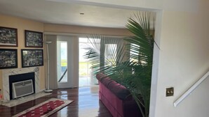 A living room with a fireplace, a large potted plant, a red sofa, and a view through a glass door to the outside.