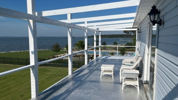 A covered porch with white railings, two white lounge chairs, and a view of the ocean and beach.