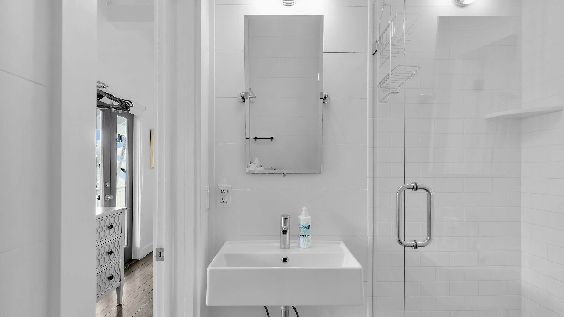 Un baño moderno con lavamanos blanco, un espejo y zona de ducha.