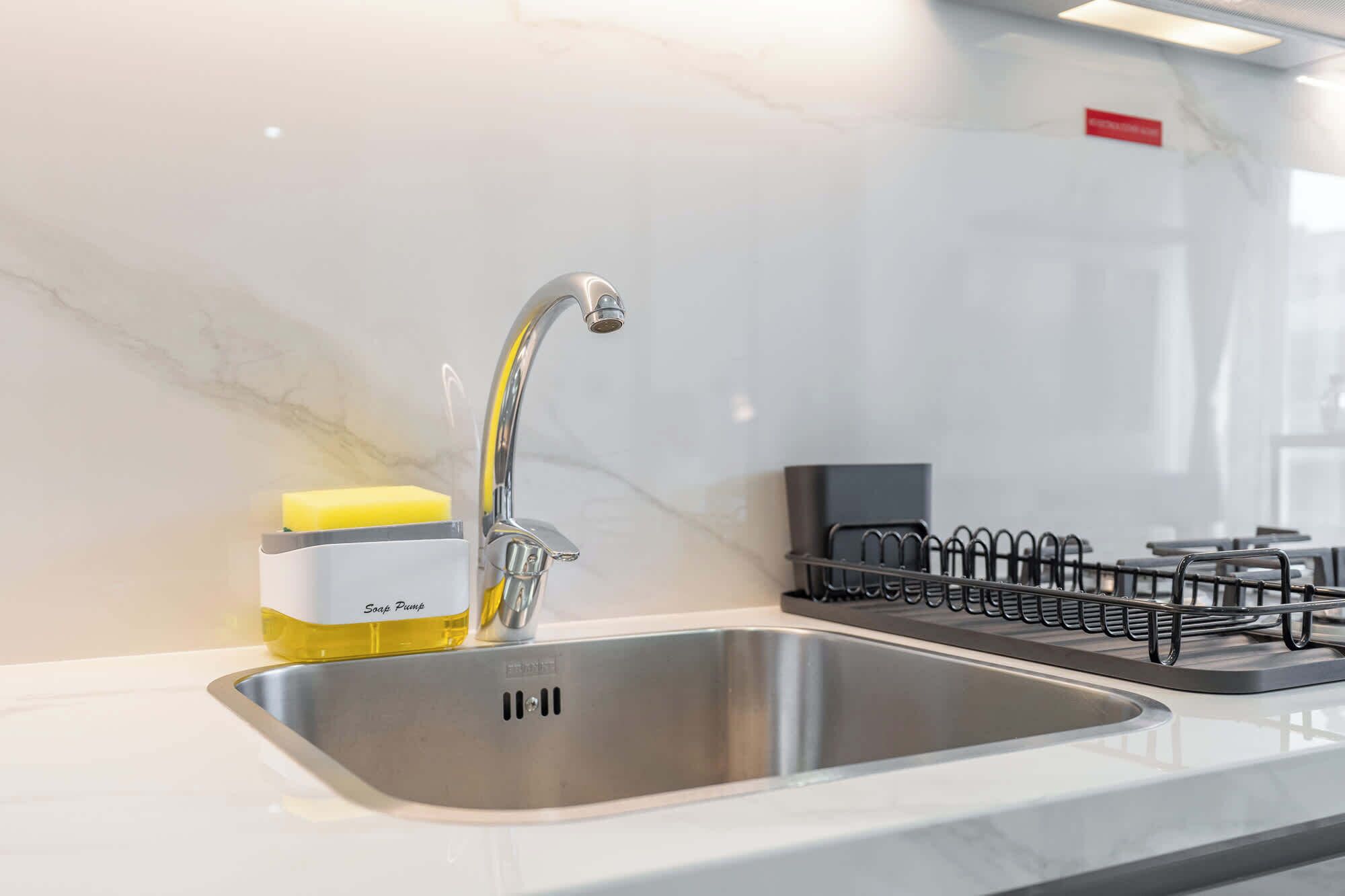 A modern kitchen with a stainless steel sink, a soap pump, and a dish drying rack.