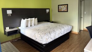 A hotel room with a large bed, a nightstand, a wall-mounted lamp, and a framed picture on the wall. - We in Heart DownTown of Columbus and Fort Moore (Columbus)
