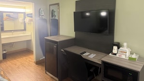 A compact hotel room with a kitchenette, a flat-screen TV mounted on the wall, a small desk with a chair, and a microwave. - We in Heart DownTown of Columbus and Fort Moore (Columbus)