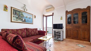 A living room with a red sofa, a small table, a TV, and a wooden cabinet. - Villa Lavinia (Positano)