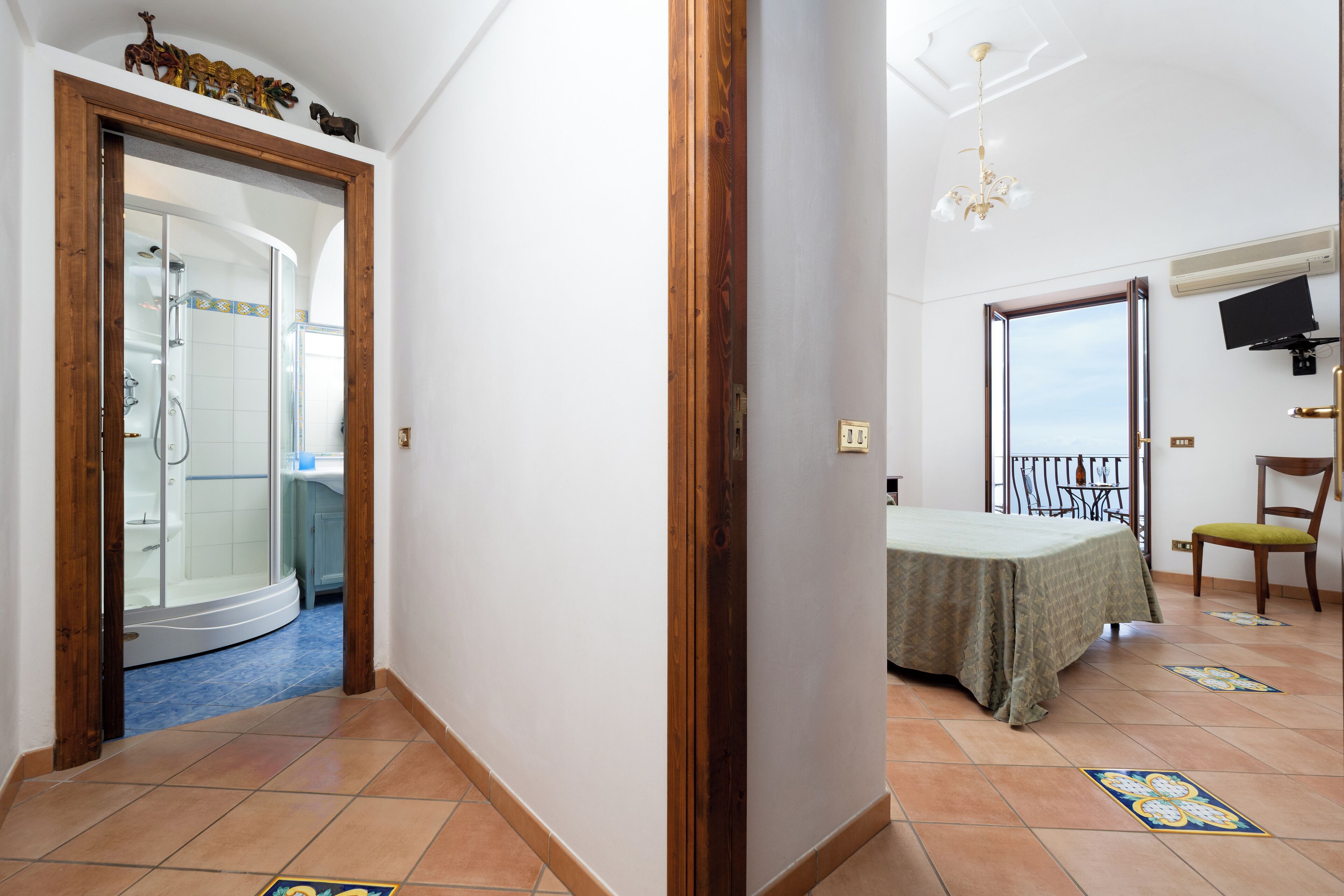 A hotel room with a curved shower, a balcony with a table and chair, and a TV mounted on the wall.