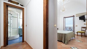 A hotel room with a curved shower, a balcony with a table and chair, and a TV mounted on the wall. - Villa Lavinia (Positano)