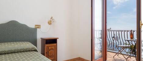 A bedroom with a bed, a nightstand, and a sliding glass door leading to a balcony with a view.