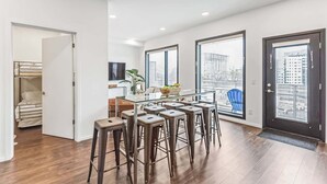 Een moderne keuken met een glazen eettafel en barstoelen, grote ramen met uitzicht over de stad, en een deur die leidt naar een berging.
