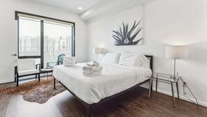 Een moderne hotelkamer met een groot bed, een glazen tafel, een stoel, een bureau en uitzicht op de stad.