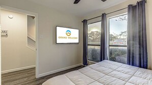 A bedroom with a bed, a television displaying 'GRAND WELCOME,' a window with curtains, and a door. - Cozy 3 BDR Condo in Horseshoe Bay, Near Marina! (Horseshoe Bay)