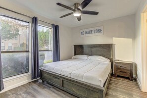 A bedroom with a bed, a ceiling fan, a window with curtains, a bedside table, and a sign that reads 'NO WAKE ZONE'. - Cozy 3 BDR Condo in Horseshoe Bay, Near Marina! (Horseshoe Bay)