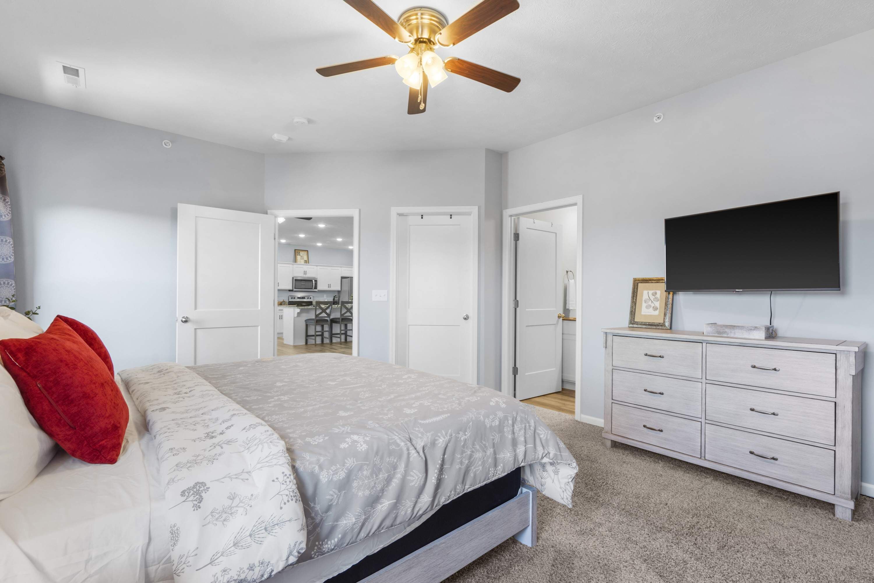 A bedroom with a bed, a ceiling fan, a dresser, and a TV.