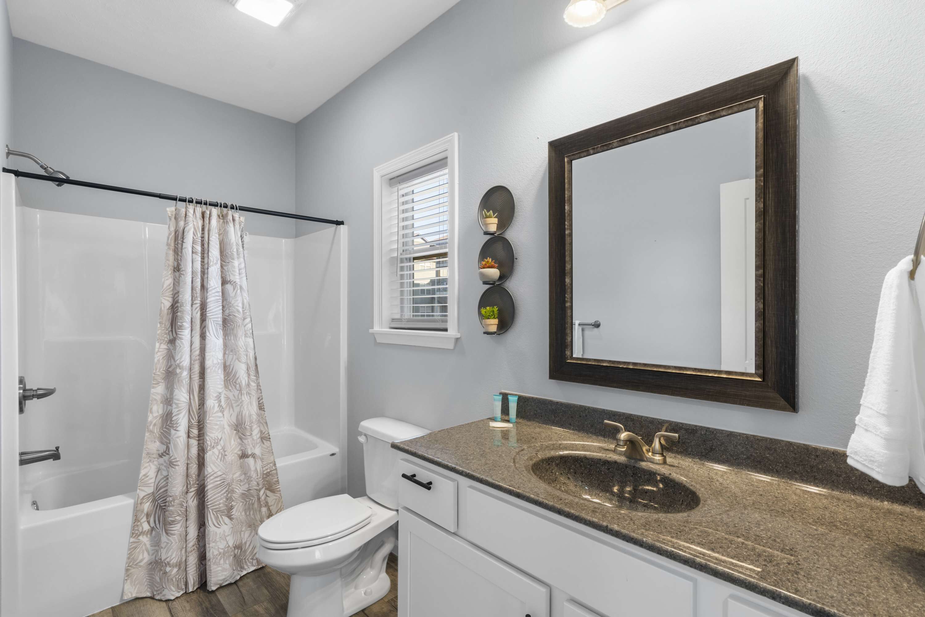 A bathroom with a shower, toilet, sink, and a large mirror.