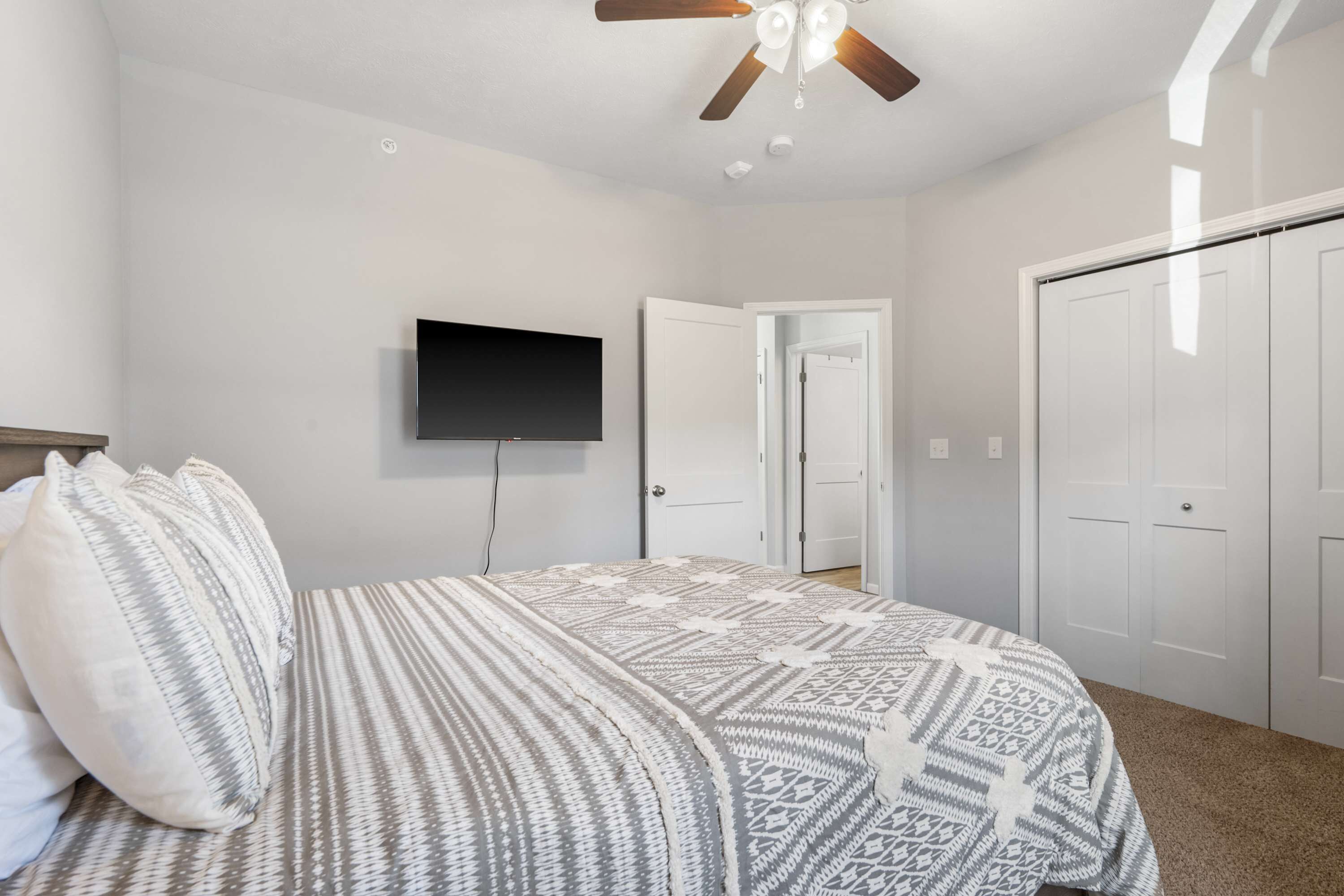 Une chambre à coucher avec un lit, un ventilateur de plafond, une télévision et une armoire.