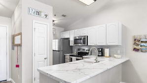 A modern kitchen with white cabinetry, a marble countertop, stainless steel appliances, and a small island with a sink. - Calm Waters Condo – Sleeps 4 (Branson)