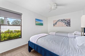 A bedroom with two beds, a ceiling fan, a window with a view of greenery, and two wall-mounted artworks. - Heated Pool ,Mini Golf, Game Room, Near Beaches (Bradenton)