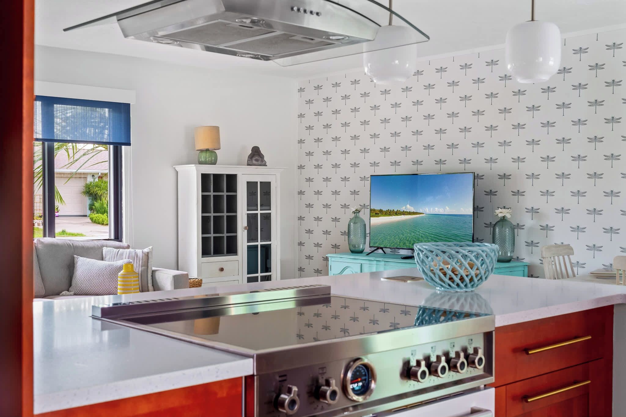 A modern kitchen with a central island, a dining area with a sofa, and a television on the wall.