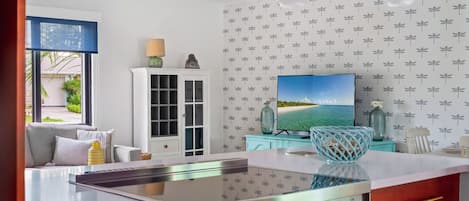 Una cocina moderna con una isla central, un área de comedor con sofá y un televisor en la pared.