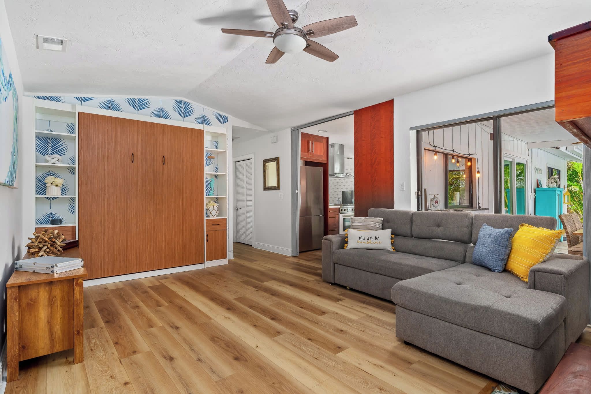 A spacious living area with a grey sectional sofa, wooden flooring, and a ceiling fan.