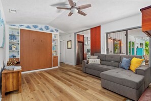 A spacious living area with a grey sectional sofa, wooden flooring, and a ceiling fan.