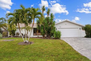 A single-story house with a white garage door, surrounded by a well-maintained lawn and several palm trees. - Heated Pool ,Mini Golf, Game Room, Near Beaches (Bradenton)