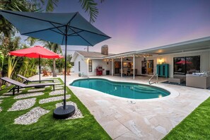 A backyard with a swimming pool, patio furniture, and a covered outdoor seating area.