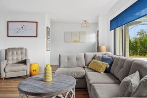 A modern living room with a grey sectional sofa, a round wooden coffee table, a grey armchair, and a yellow and white striped vase. - Heated Pool ,Mini Golf, Game Room, Near Beaches (Bradenton)