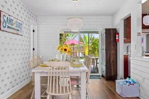 Un espace repas avec une table et des chaises blanches, un lustre et une vue sur l’extérieur.