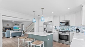 A modern kitchen with white cabinets, a central island, stainless steel appliances, and a dining area with wicker chairs. - ☀️Charming 30A Home with Private Pool-Short Walk to Beach-Jini Jim Jams☀️ (Santa Rosa Beach)