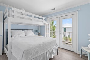 A bunk bed with a white headboard, a bedside table with a lamp, and a view of a balcony with a white railing.