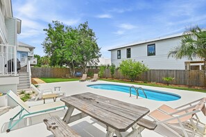 A backyard with a swimming pool, a wooden table, and lounge chairs.