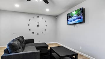 A modern living room with a grey sofa, a black coffee table, and a wall-mounted TV displaying a nature scene.