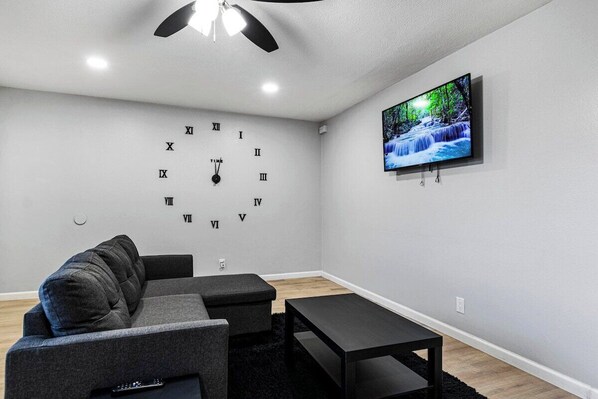 A modern living room with a grey sofa, a black coffee table, and a wall-mounted TV displaying a nature scene.