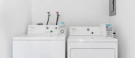 Dos lavadoras Whirlpool blancas con paneles de control, mangueras y un medidor de agua sobre una pared blanca.