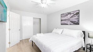 A bedroom with a bed, a ceiling fan, a wall-mounted TV, and a framed picture.