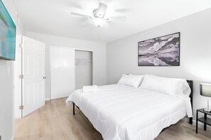 Un dormitorio con cama, ventilador de techo, televisor montado en la pared y un cuadro enmarcado.