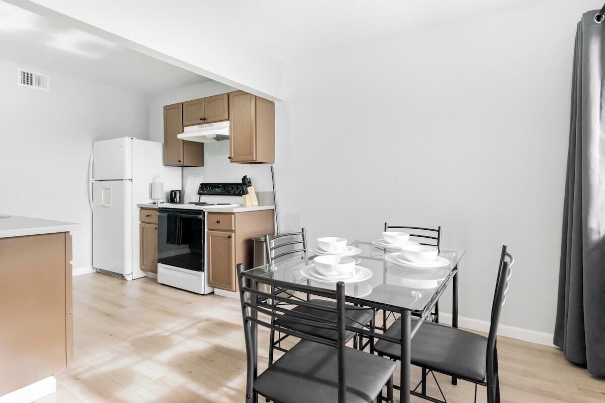 A modern kitchen with a dining table set for four, wooden cabinets, and a white refrigerator.