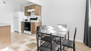 A modern kitchen with a dining table set for four, wooden cabinets, and a white refrigerator.