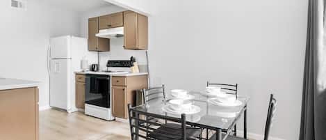A modern kitchen with a dining table set for four, wooden cabinets, and a white refrigerator.