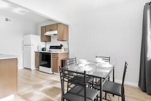 Una cocina moderna con una mesa de comedor preparada para cuatro personas, armarios de madera y un refrigerador blanco.