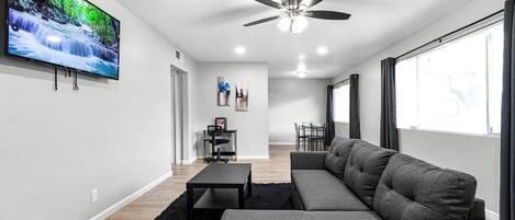 A modern living room with a flat-screen TV, a ceiling fan, a sofa, a coffee table, and a dining area.