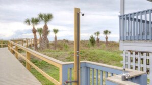 Une promenade en bois dotée d’une rambarde, menant à un bâtiment entouré d’une clôture bleue et équipé d’une caméra de surveillance.