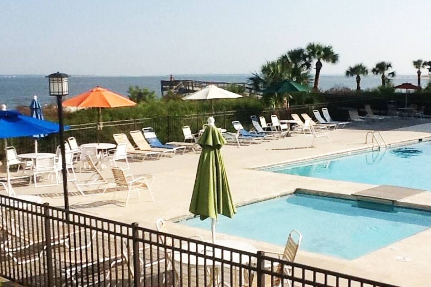 A pool area with lounge chairs and umbrellas, a clear view of the ocean, and a fenced pool.