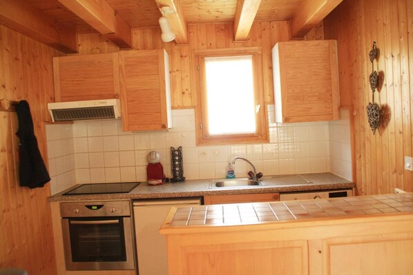 A kitchen with wooden cabinets, a stove, a sink, and a window. - Chalet in La Béchigne with Valley Views (Châtel)