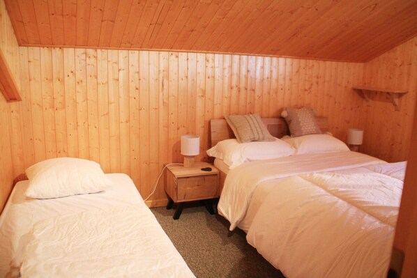 A wooden-paneled room with two beds, each with white bedding. There is a nightstand with a lamp between the beds. - Chalet in La Béchigne with Valley Views (Châtel)