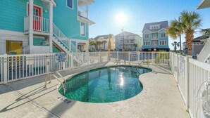 A swimming pool surrounded by a white fence, with a turquoise building and a balcony on the left. - A Little Piece Of Heaven-5BR-2nd Row-Pet Friendly (North Myrtle Beach)