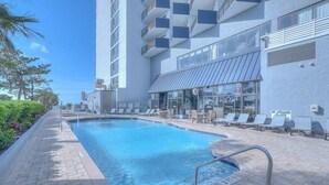 A swimming pool with lounge chairs and a building with balconies.