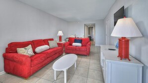 A living room with two red sofas, a white coffee table, and a red lamp on a white cabinet.