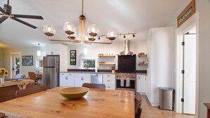 Una cocina moderna con una mesa de comedor de madera, electrodomésticos de acero inoxidable e iluminación colgante.