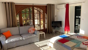 A room with a striped sofa, a bed with a colorful quilt, a TV on a stand, and a sliding glass door leading to a balcony. - Detached south-facing studio with swimming pool, property overlooking Toulon harbour  (Toulon)